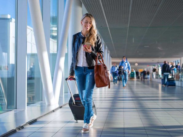 woman smiling and looking at her mobile device while walking through an airport terminal