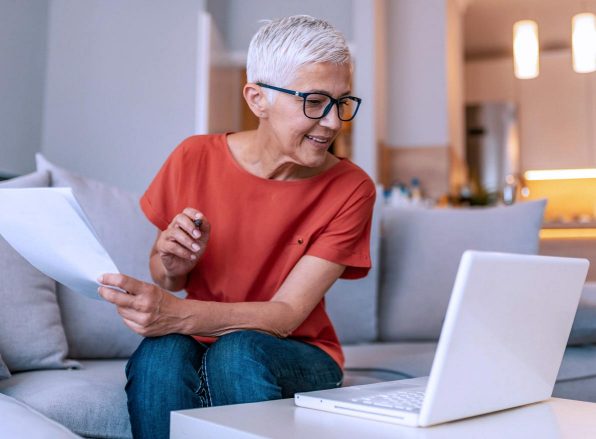 Woman holding paper while smiling and looking at a laptop